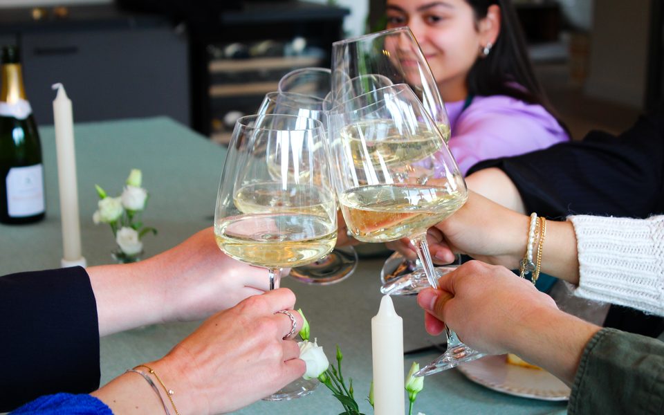 Gasten proosten met glazen witte wijn aan een gedekte tafel